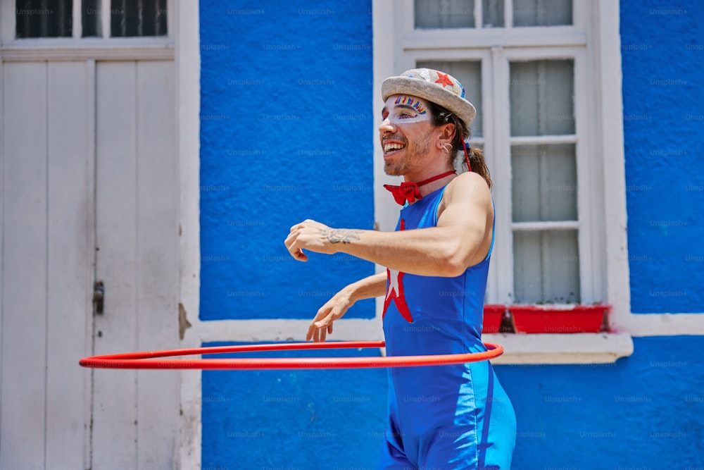 um homem de macacão azul brincando com um bambolê vermelho