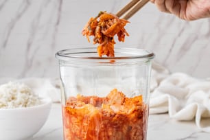 a person holding chopsticks above a jar of food