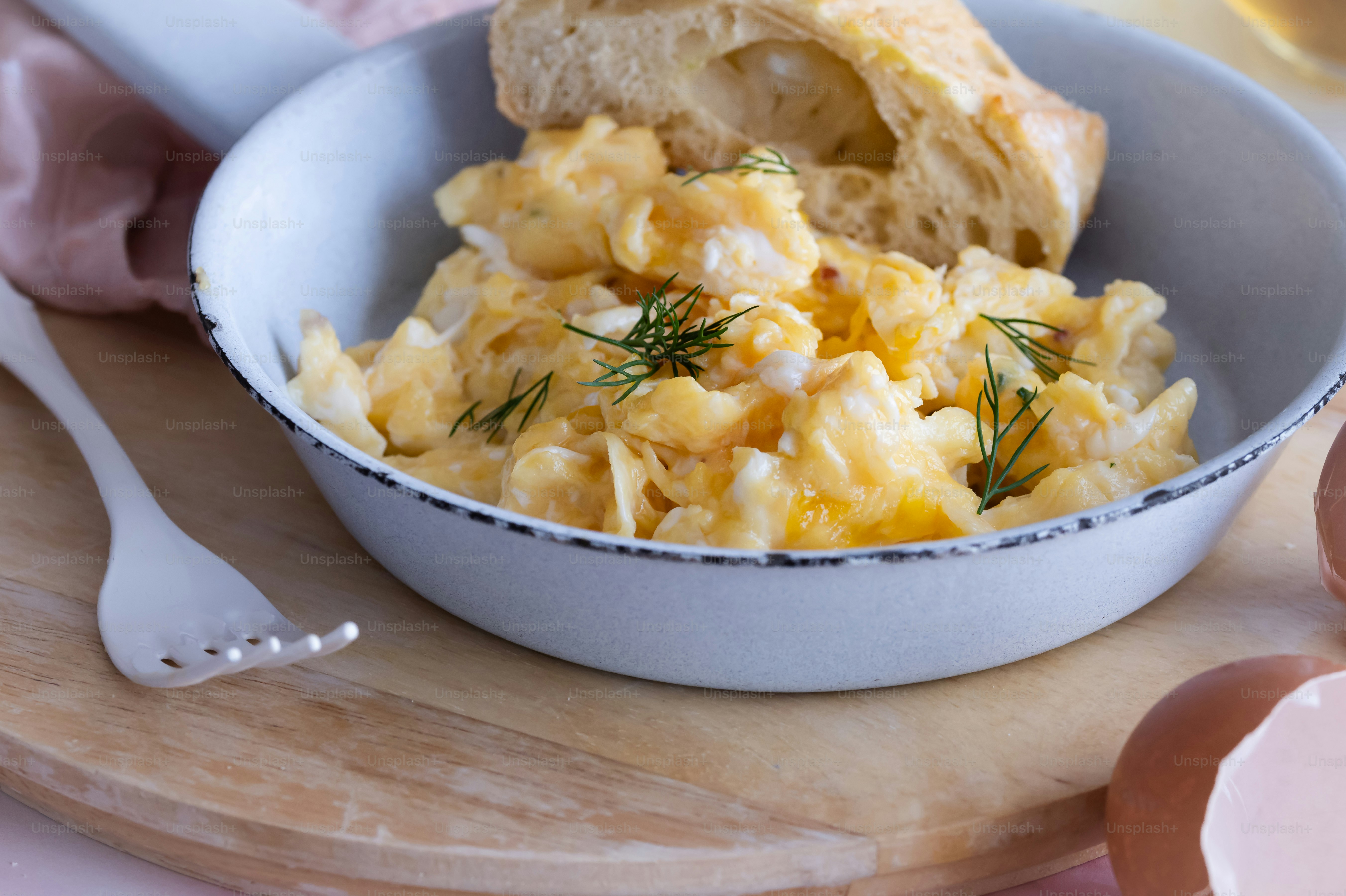 a bowl of eggs and a piece of bread on a cutting board
