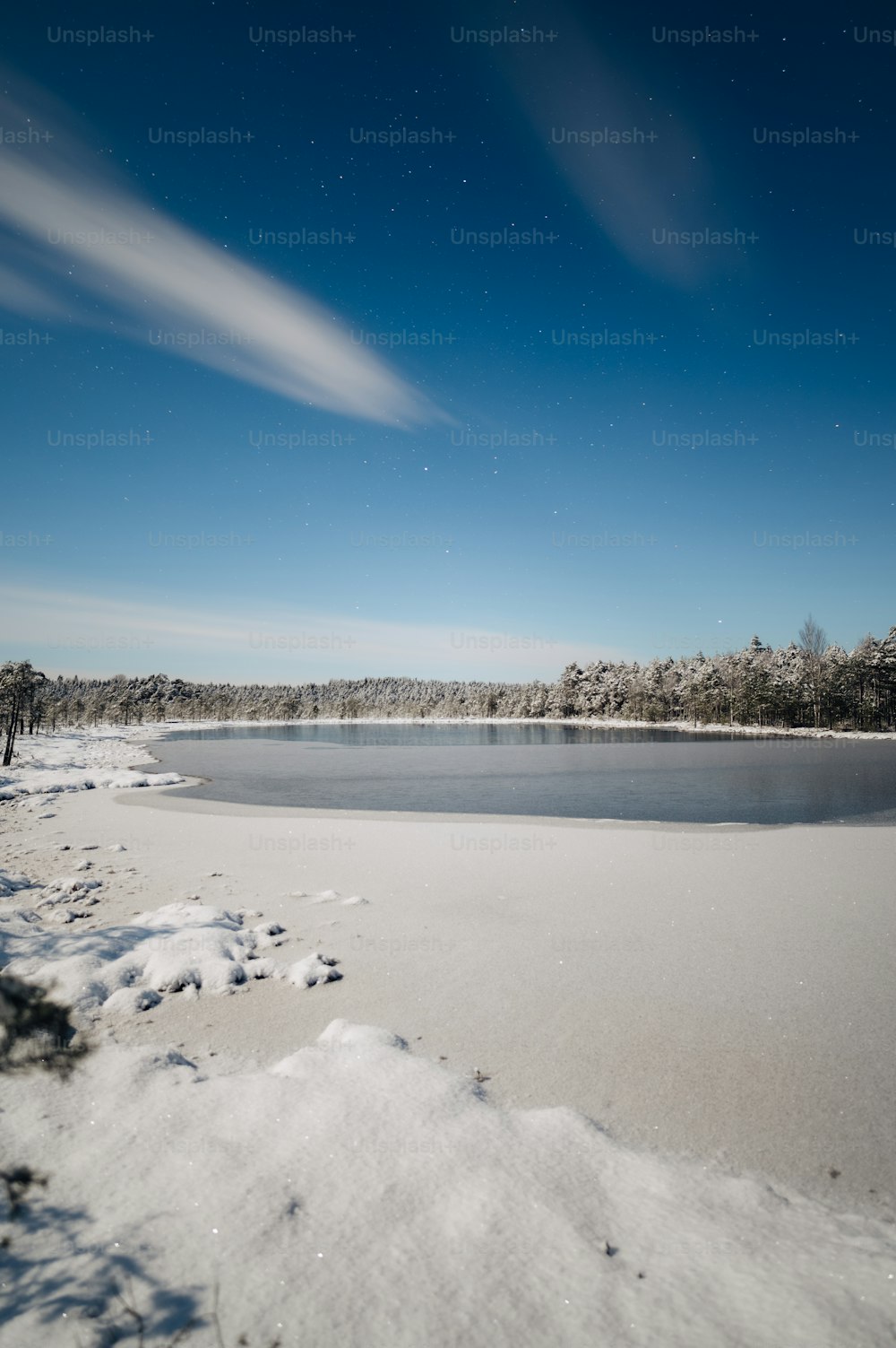 a lake surrounded by snow and trees under a blue sky