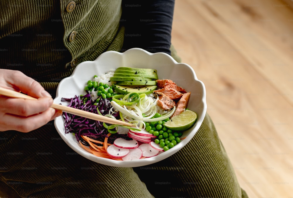 a person holding a bowl of food with chopsticks