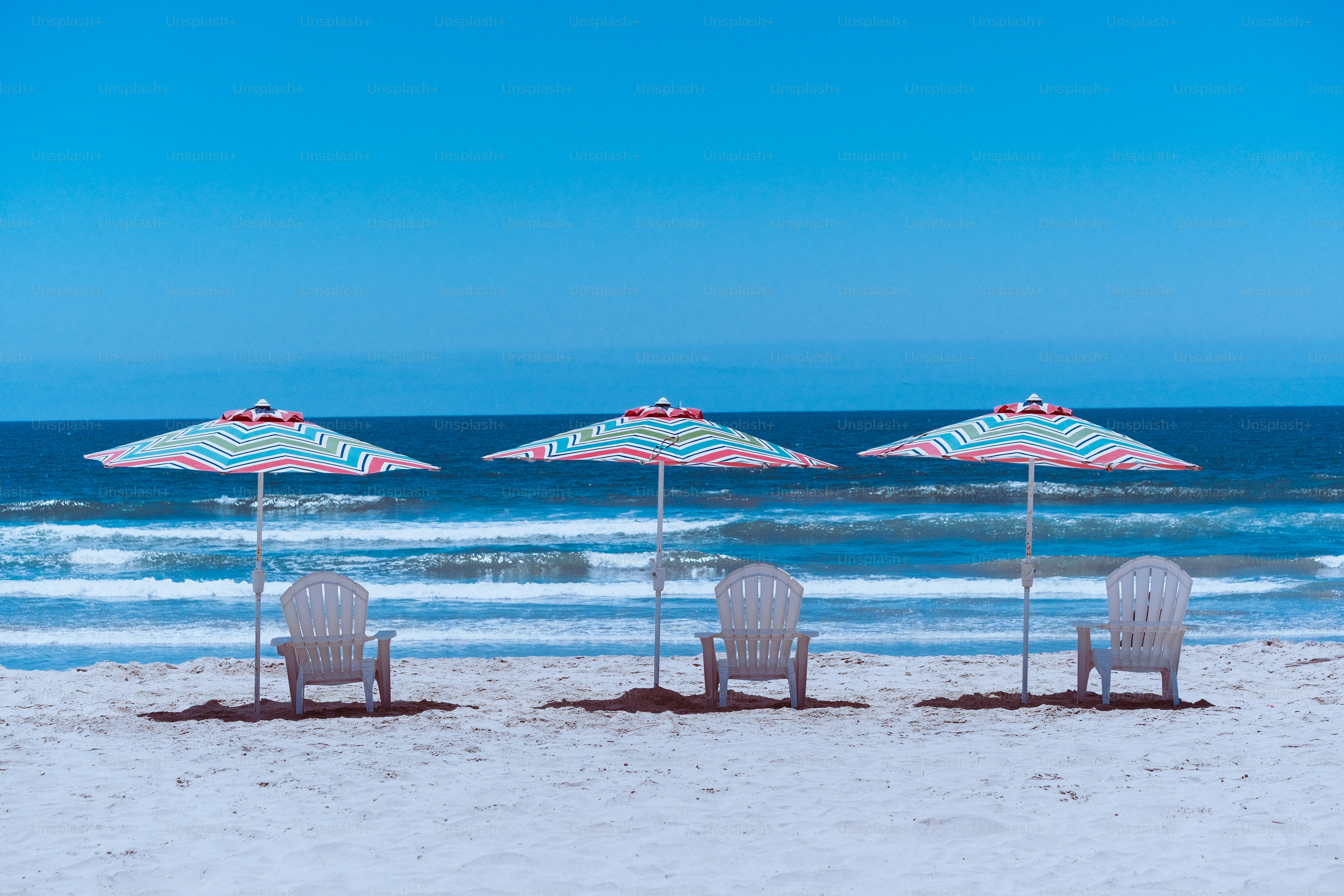 three lawn chairs and two umbrellas on a beach