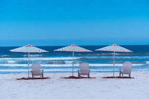 해변에 잔디 의자 3 개와 우산 2 개