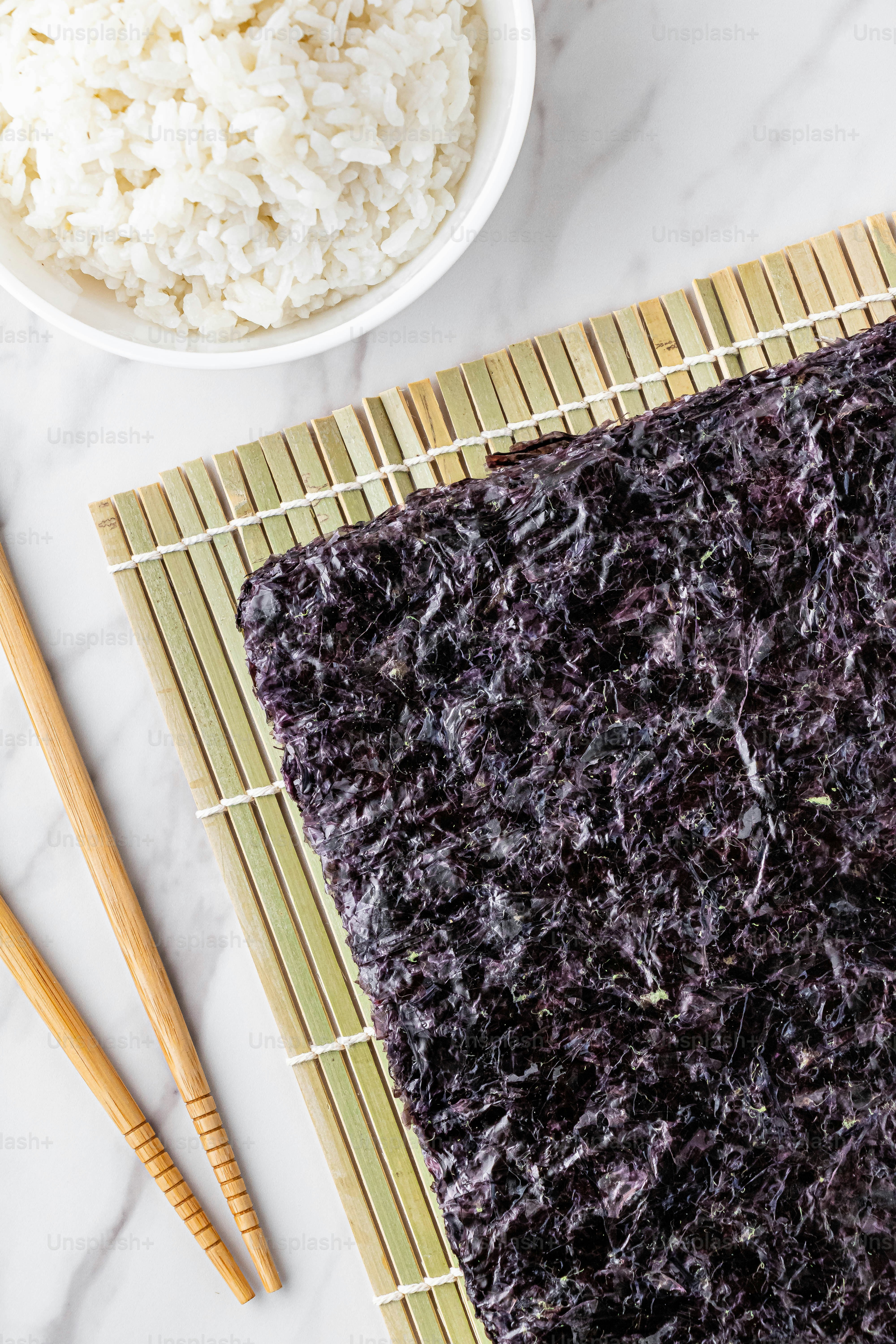 a bowl of rice and chopsticks on a bamboo mat