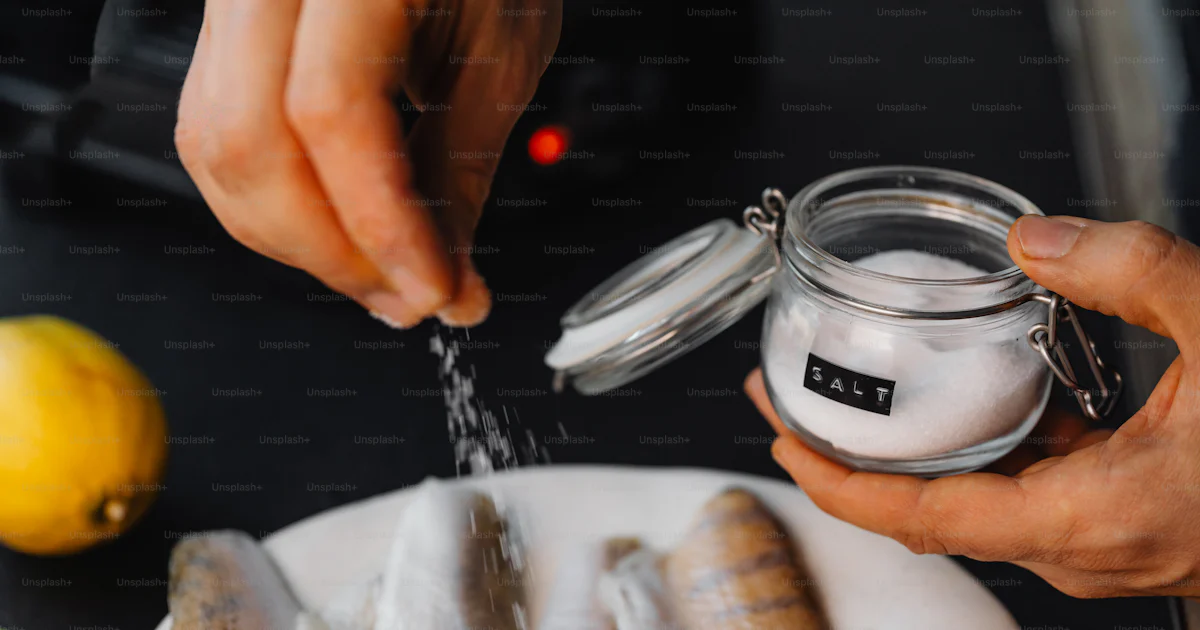 A person sprinkling salt onto fish on a plate photo – Food Image on ...