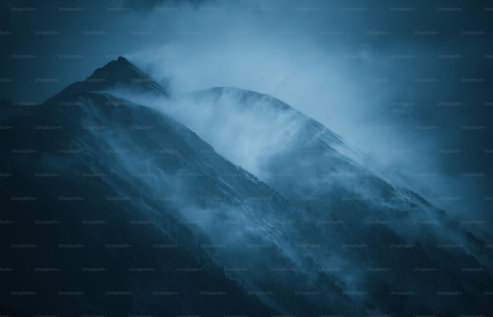 a very tall mountain covered in fog under a cloudy sky