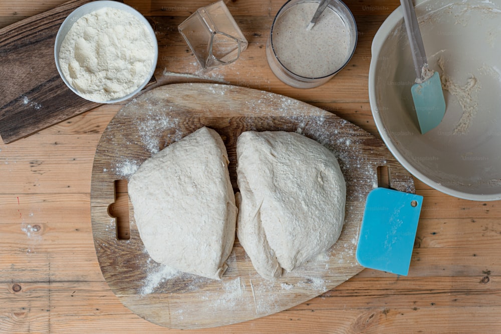 a wooden cutting board topped with dough next to a bowl of flour