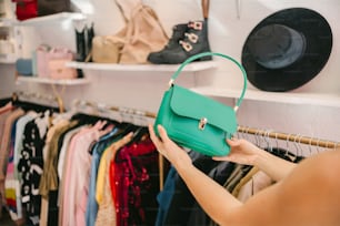 a woman holding a green purse in front of a rack of clothes