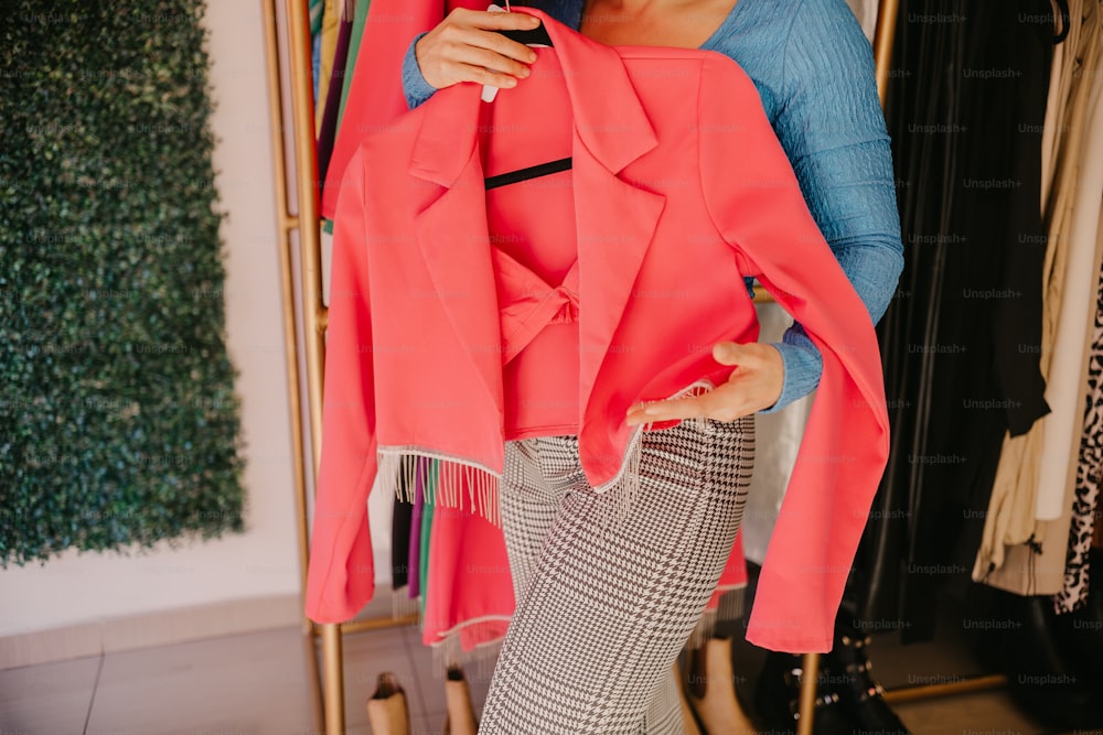 a woman holding a pink coat in front of a mirror