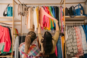 a couple of women standing in front of a rack of clothes