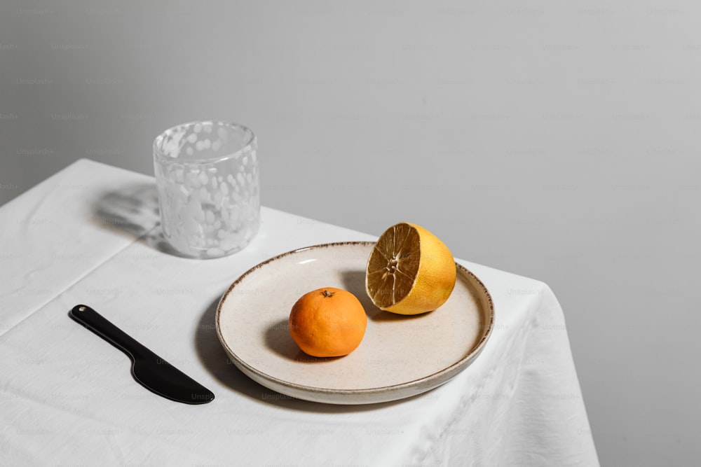 a white table with a plate of oranges and a glass of water