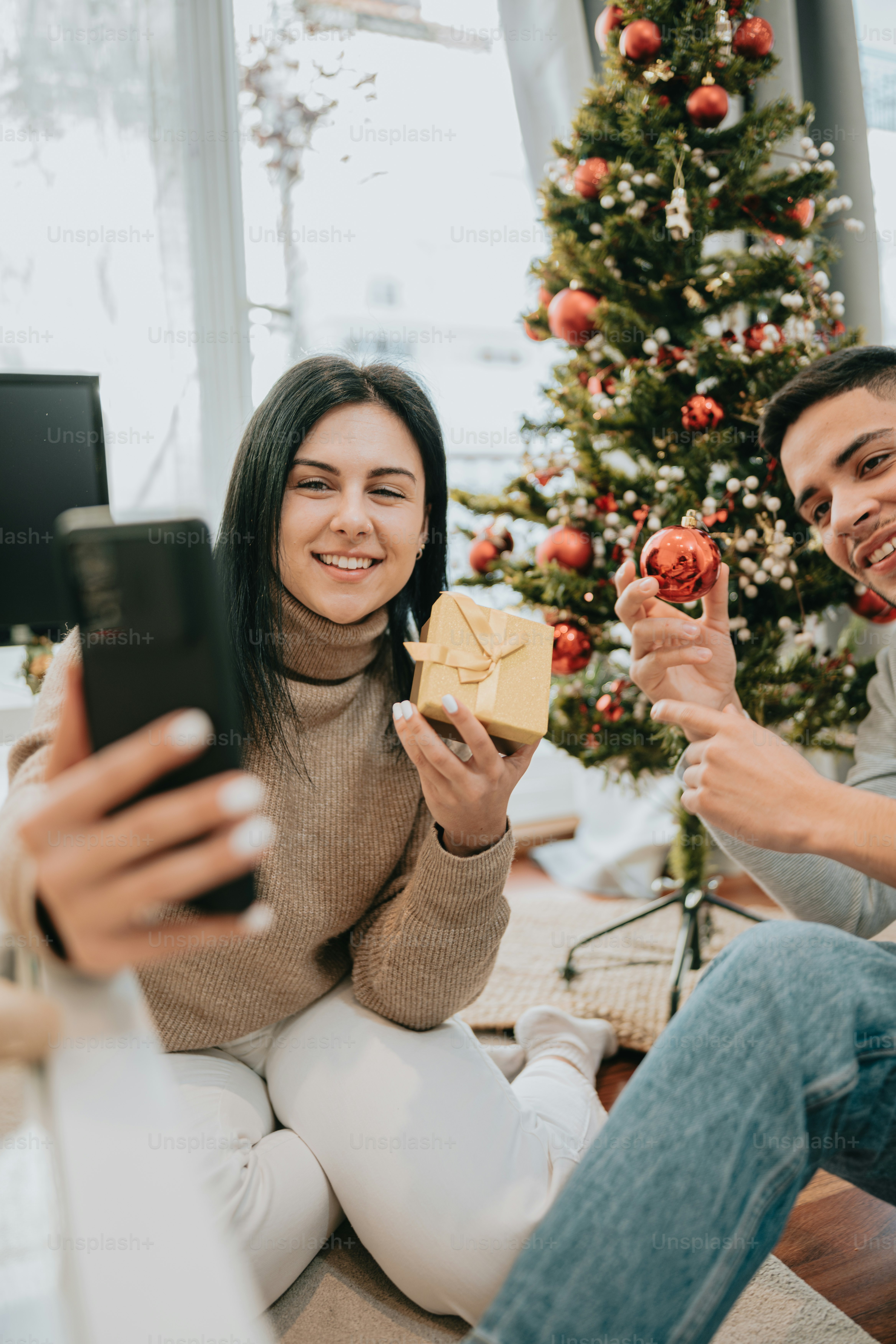 un homme et une femme assis sur le sol avec un arbre de Noël en arrière-plan