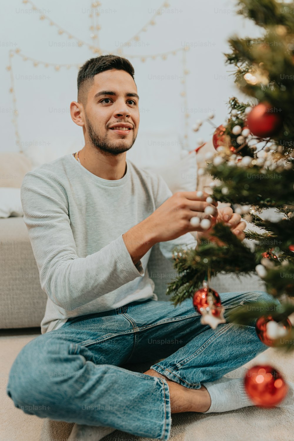 a man sitting on the floor next to a christmas tree