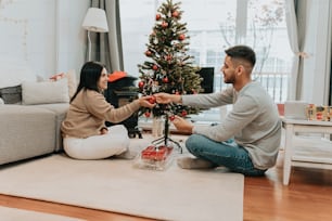 a man and woman sitting on the floor near a christmas tree