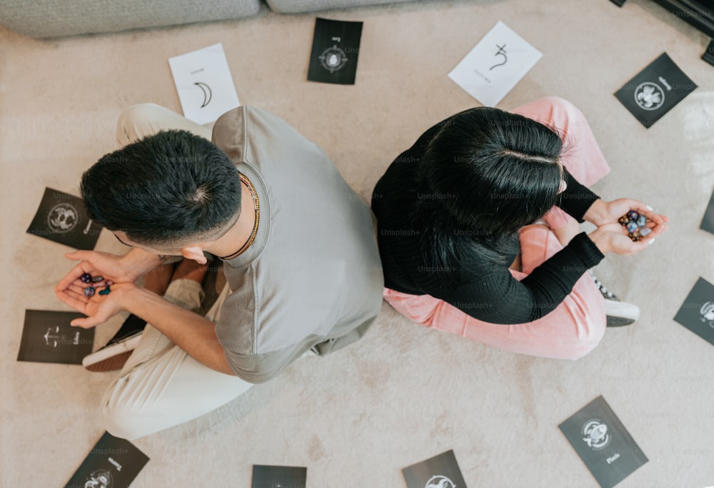 a man and a woman sitting on the floor looking at their cell phones