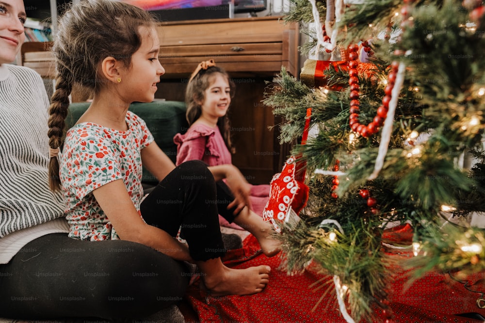 a little girl sitting next to a christmas tree
