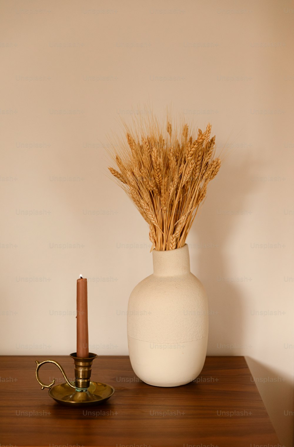a white vase with a candle and some dry grass in it