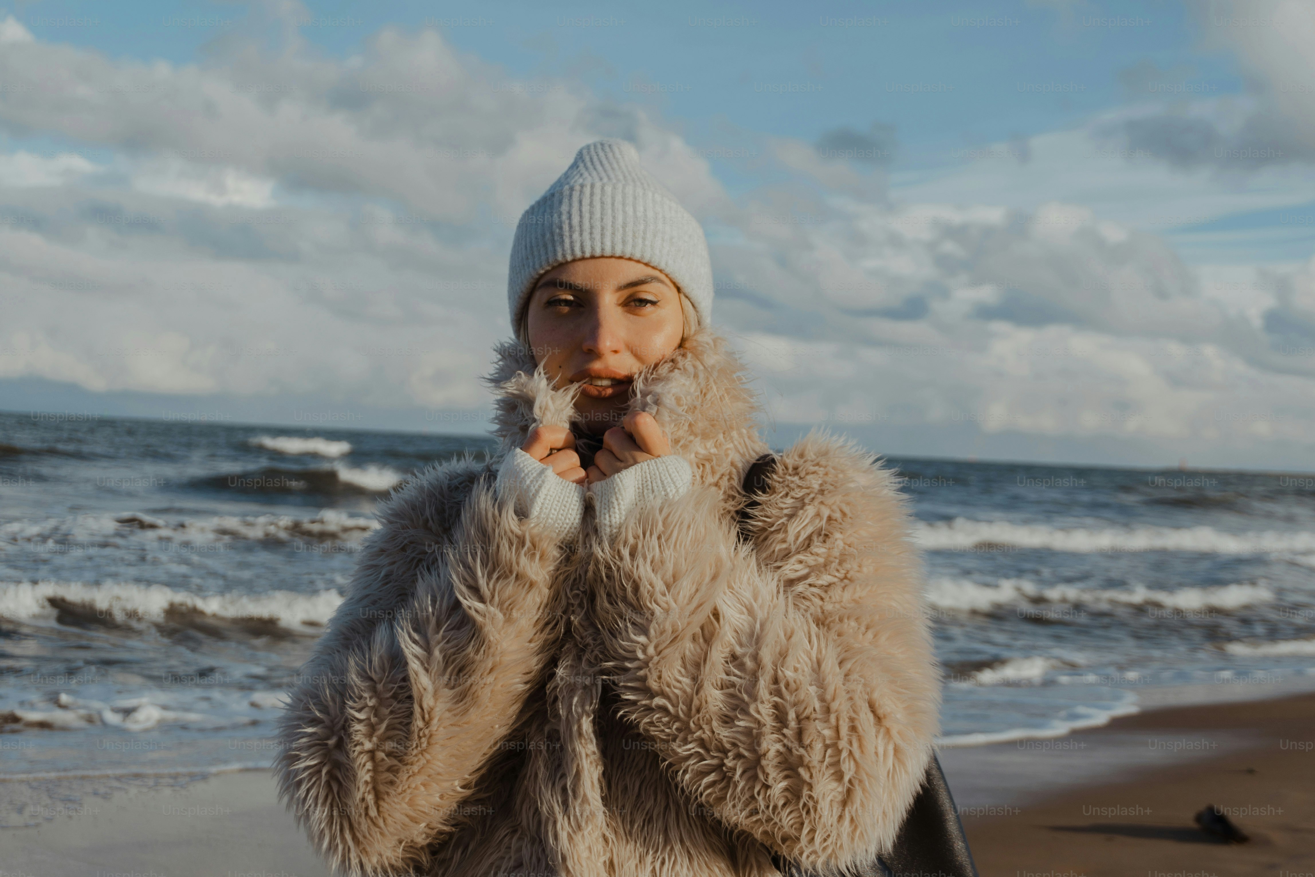 a woman in a fur coat standing on a beach
