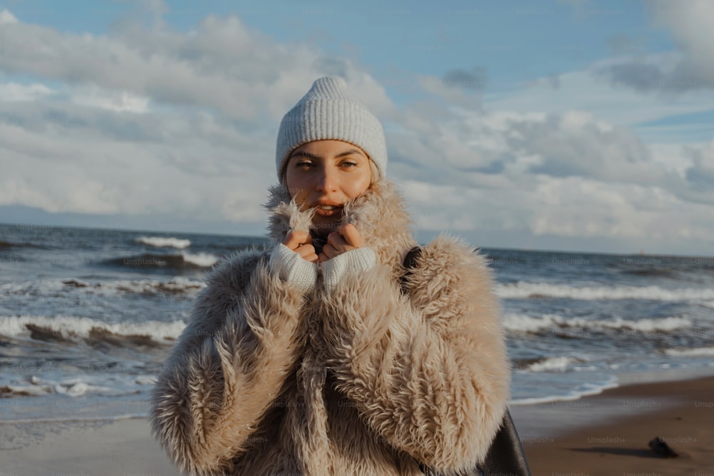a woman in a fur coat standing on a beach
