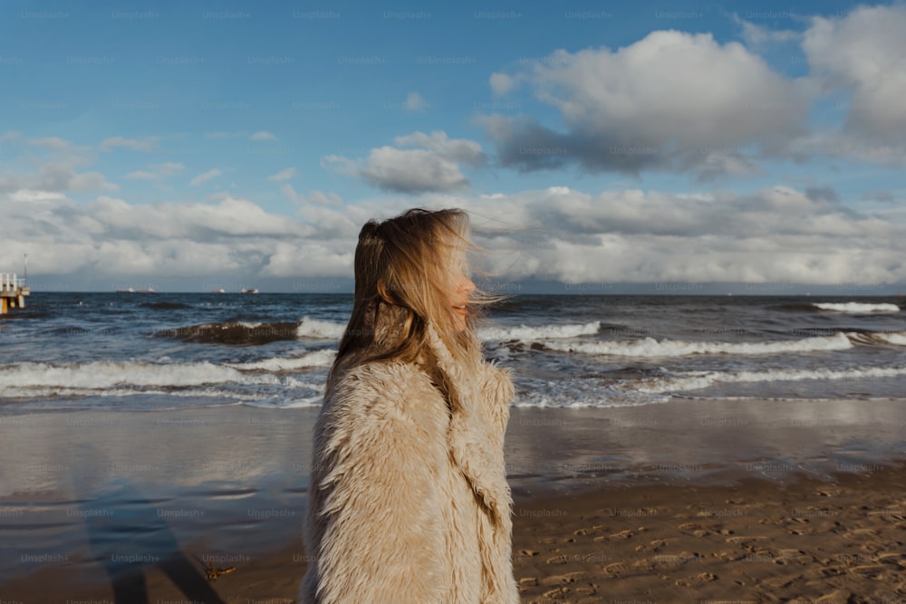 una donna in piedi in cima a una spiaggia sabbiosa vicino all'oceano