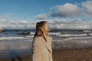une femme debout au sommet d’une plage de sable à côté de l’océan