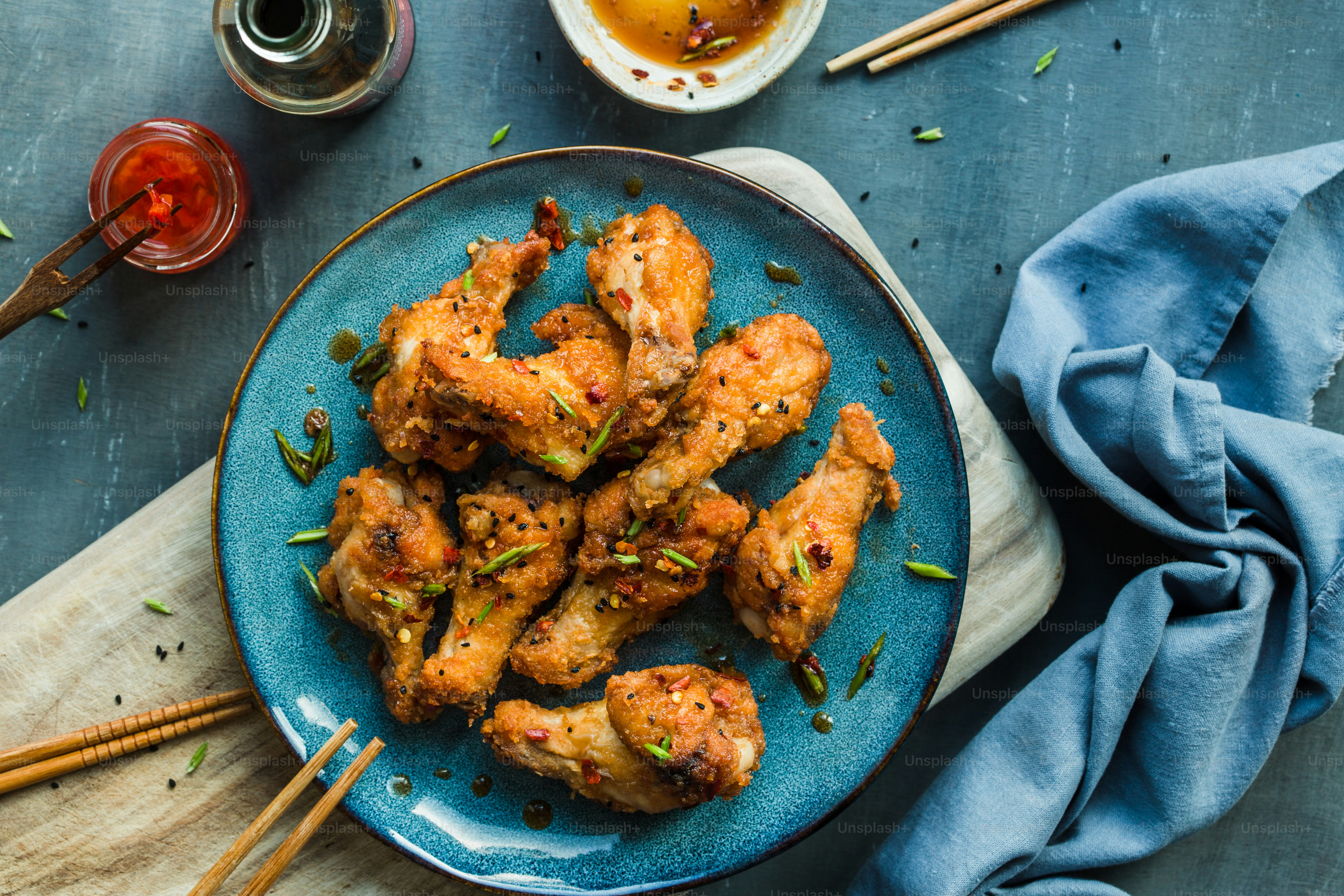 a blue plate topped with chicken wings next to a bowl of dipping sauce