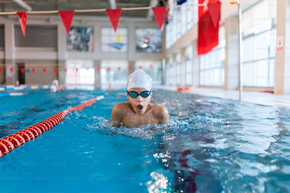 a young boy swimming in a pool wearing a swimming cap and goggles