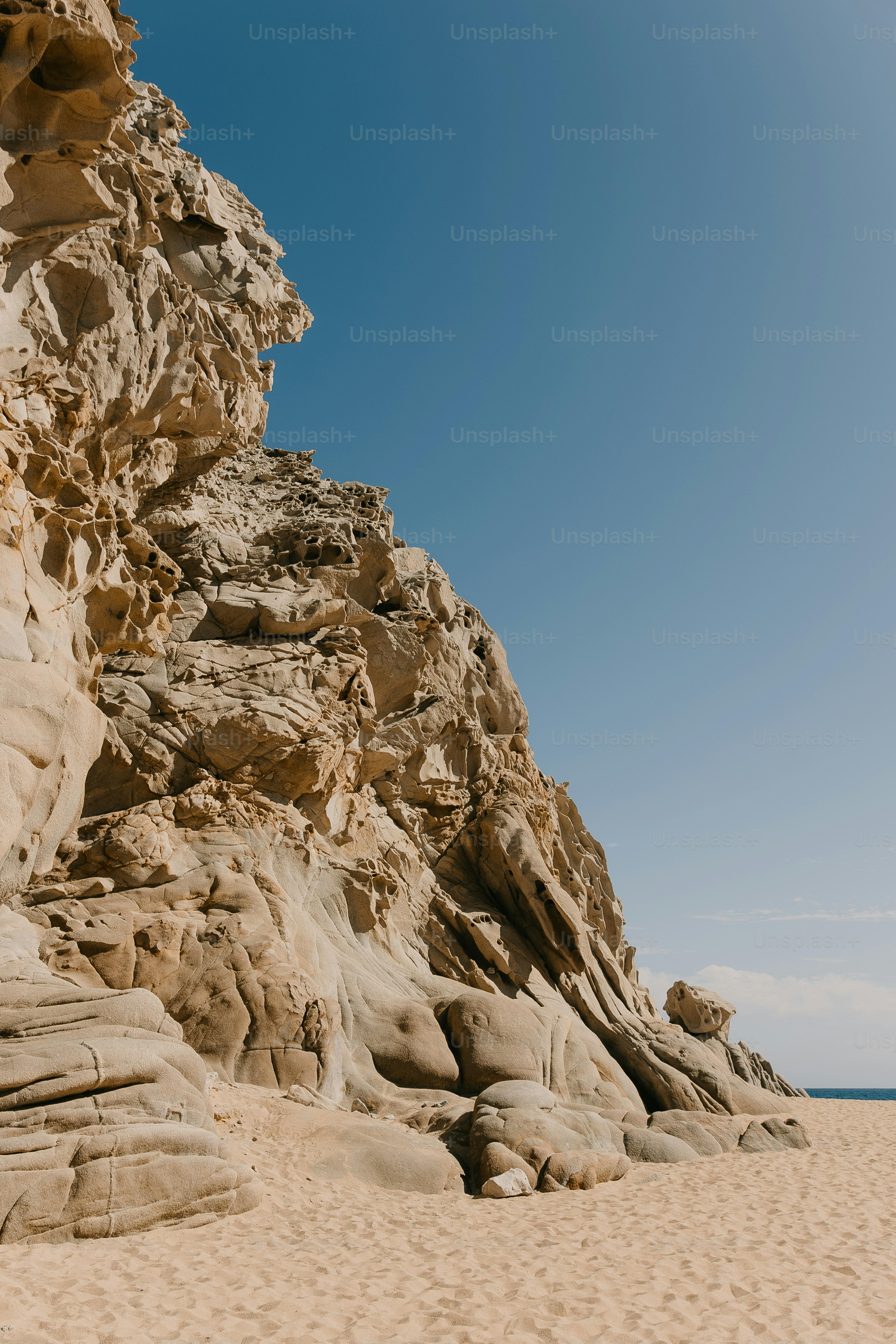 A sandy beach with a large rock formation on top of it photo – Sand ...