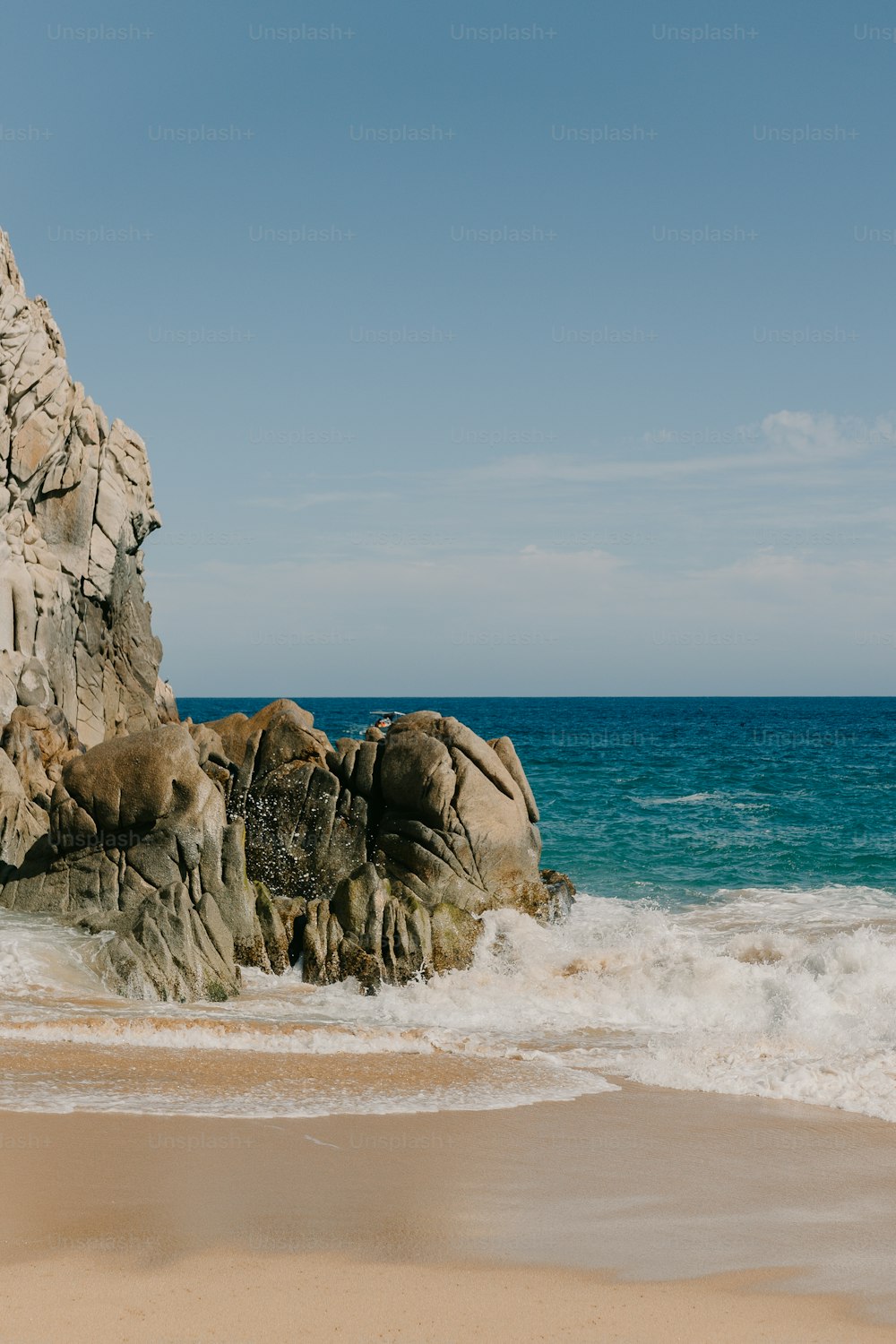 ein großer Felsen, der neben einem Strand aus dem Meer ragt