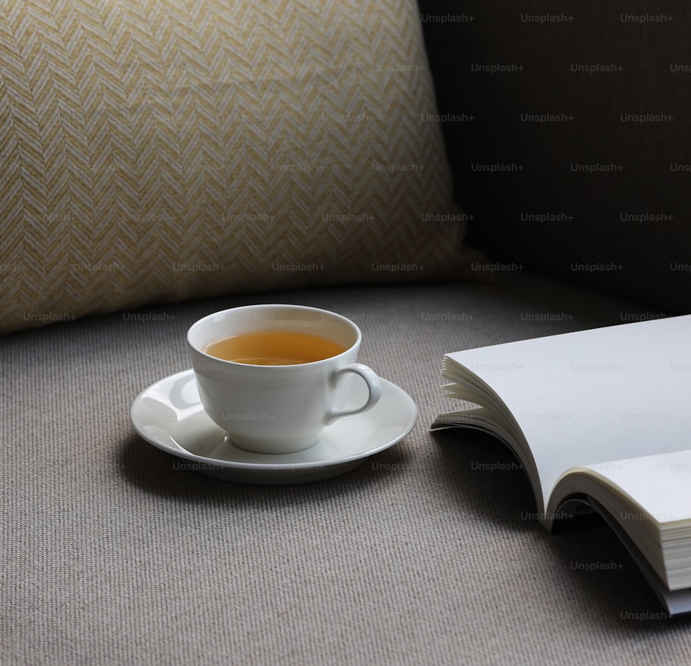 Eine Tasse Tee steht auf einer Untertasse neben einem aufgeschlagenen Buch