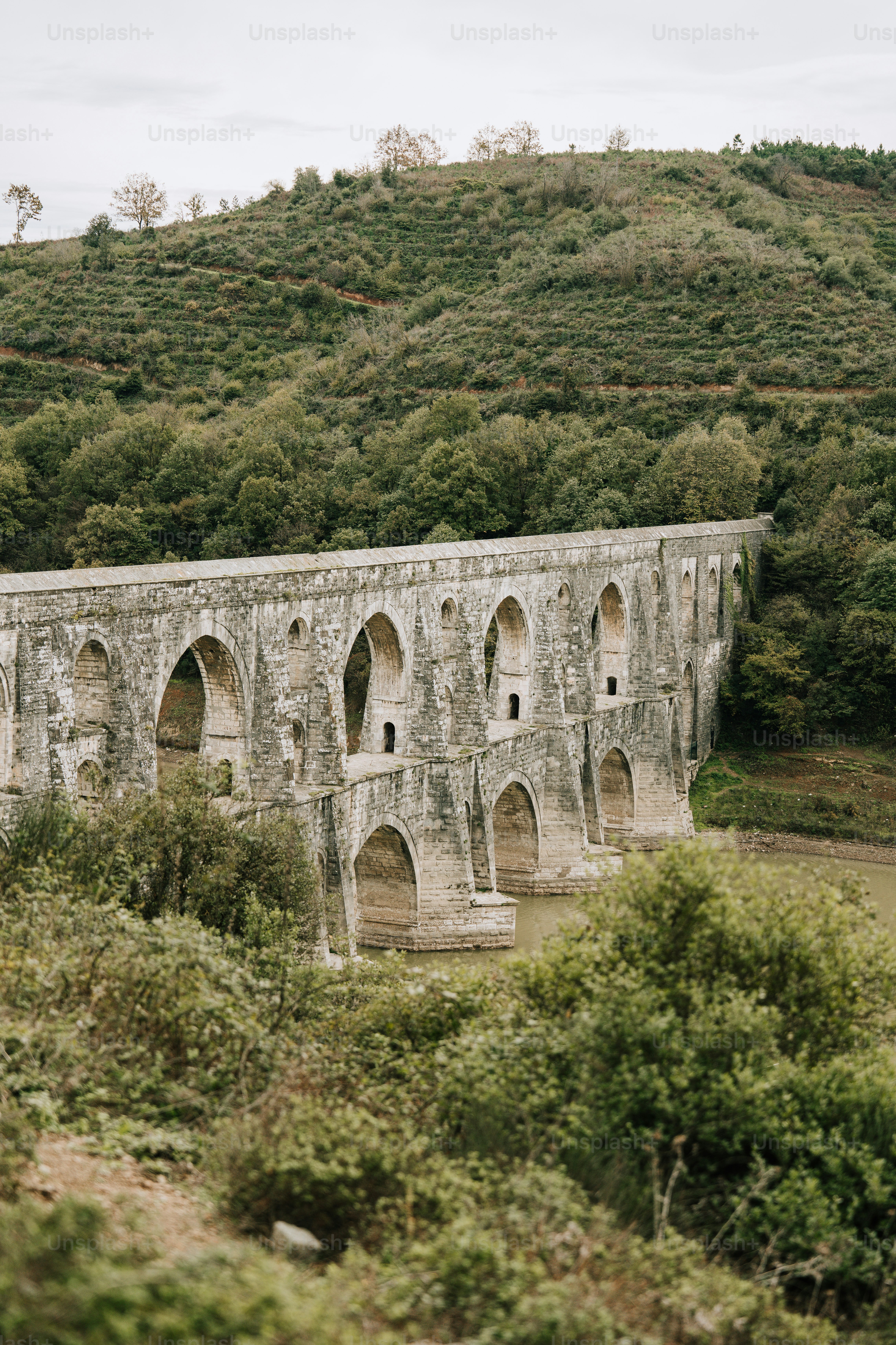 eine steinerne Brücke über einen Fluss vor einem üppig grünen Hügel