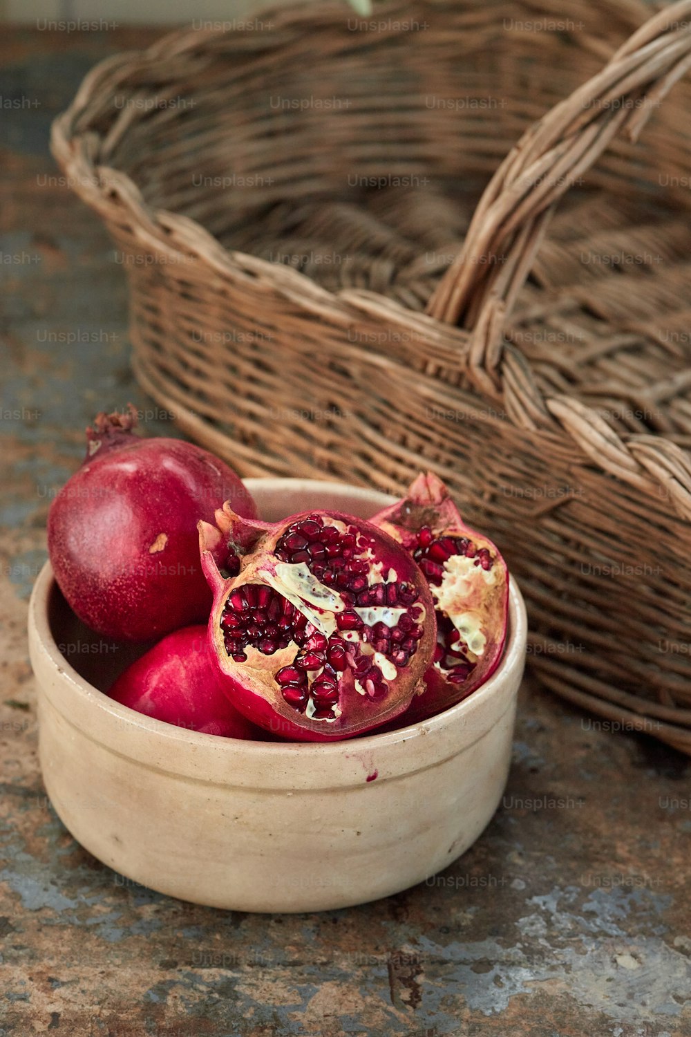 a wooden bowl filled with pomegranate next to a wicker basket