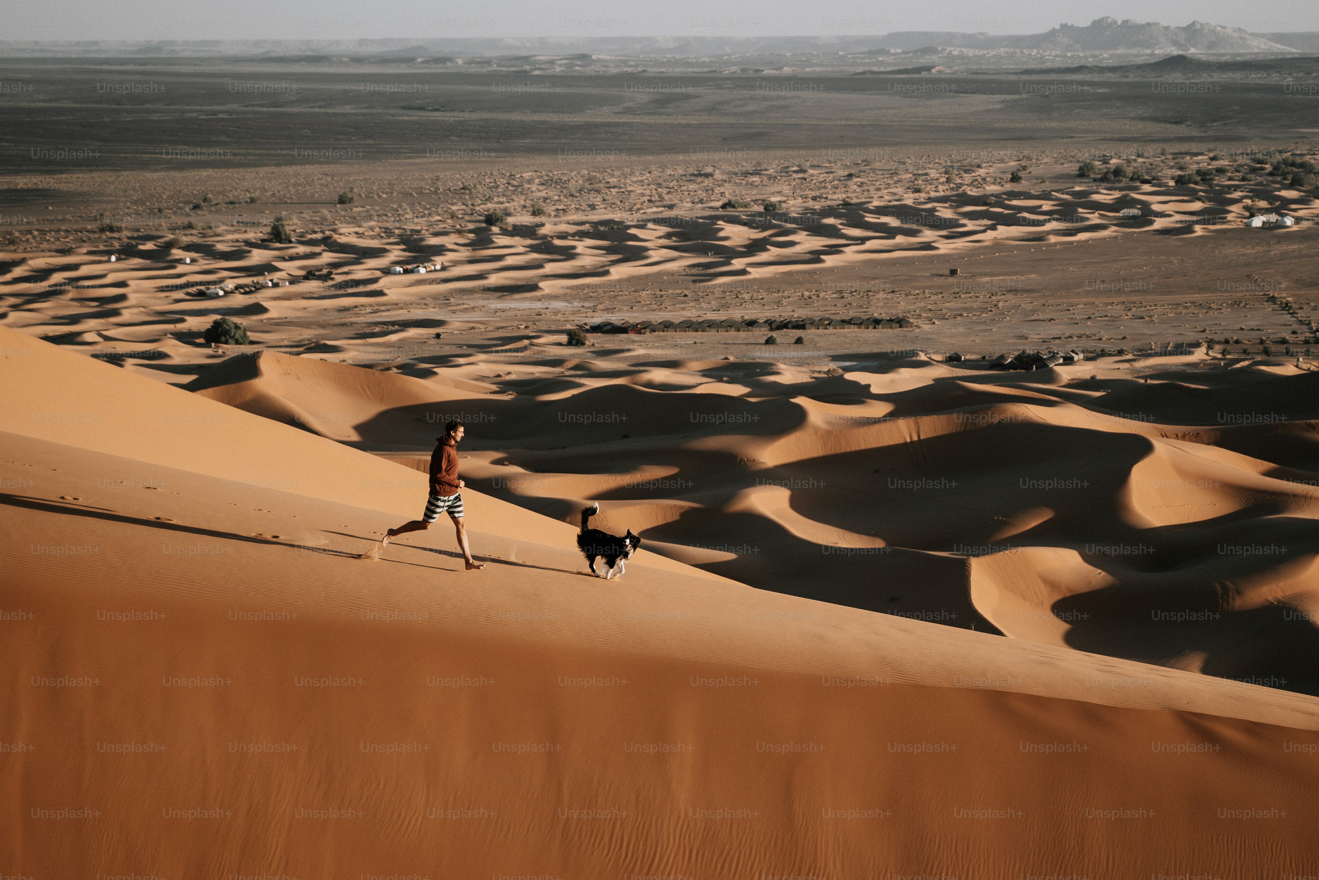 A lone explorer walking through vast desert dunes toward an ancient stone arch half-buried in sand.
