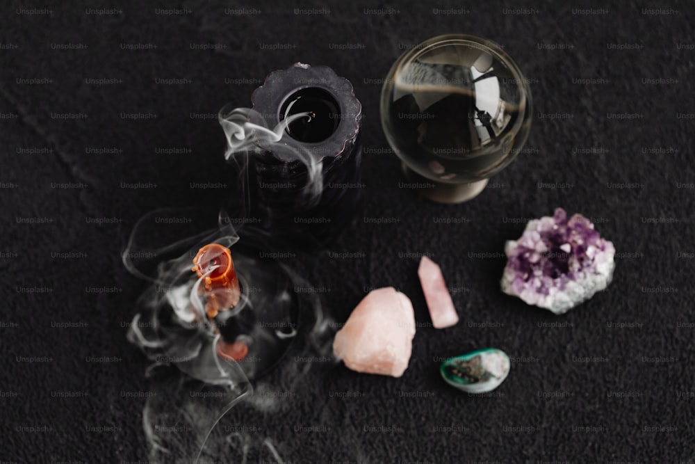 Ein Glas Flüssigkeit, eine Pfeife und ein paar Steine auf einer schwarzen Oberfläche