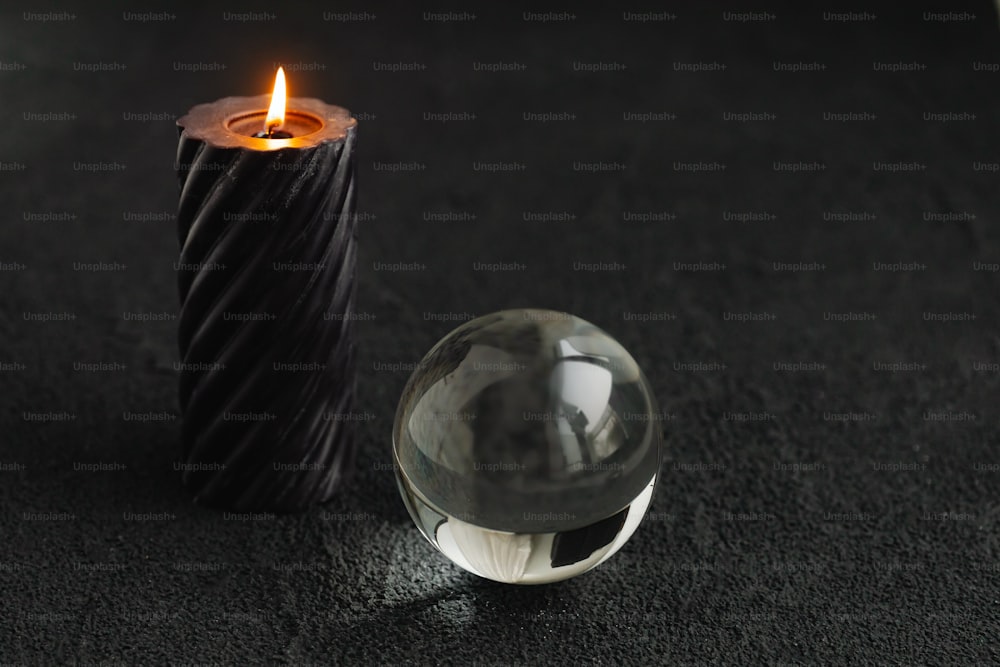 uma bola de vidro sentada ao lado de uma vela em uma superfície preta