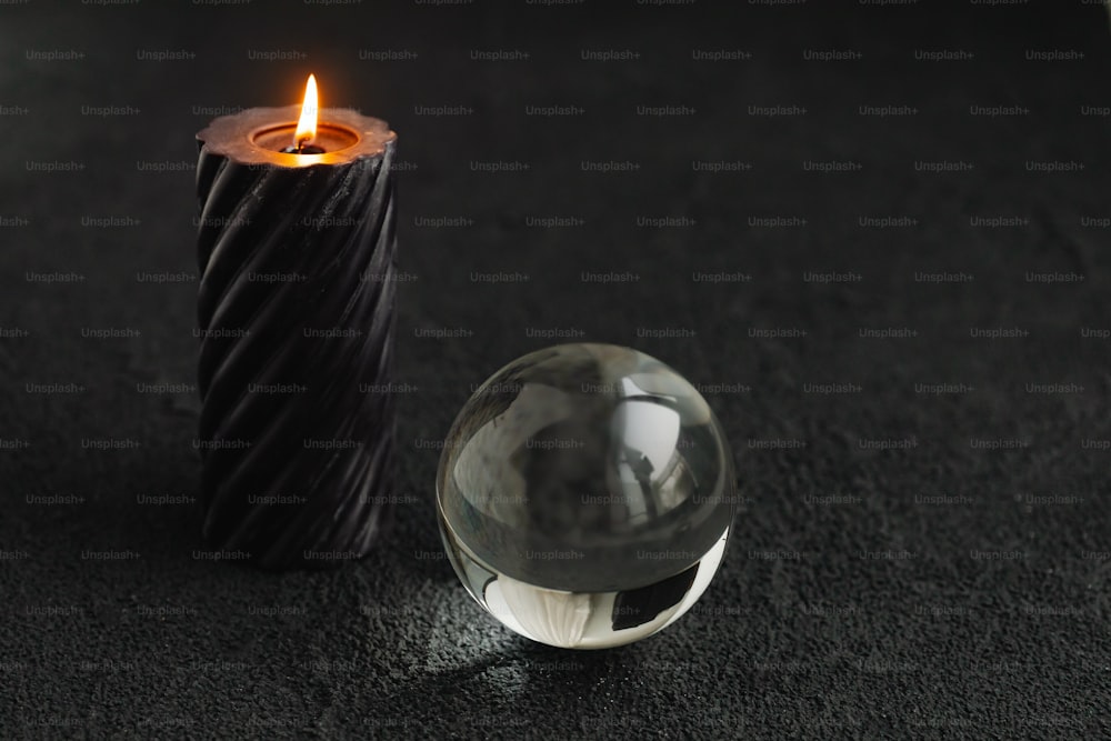 a glass ball sitting next to a candle on a black surface