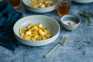 a white bowl filled with pasta next to a cup of tea