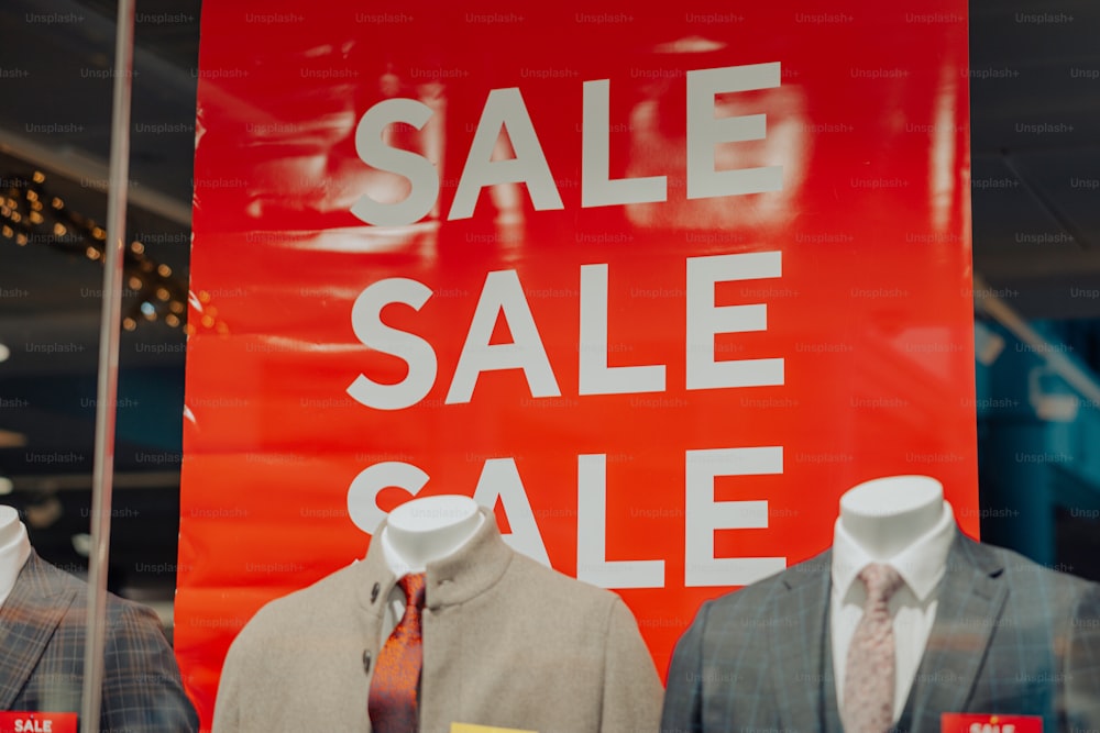 Un letrero rojo de venta detrás de dos maniquíes vestidos de traje