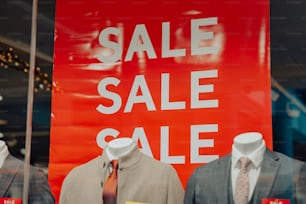 un cartello rosso di vendita dietro due manichini in giacca e cravatta