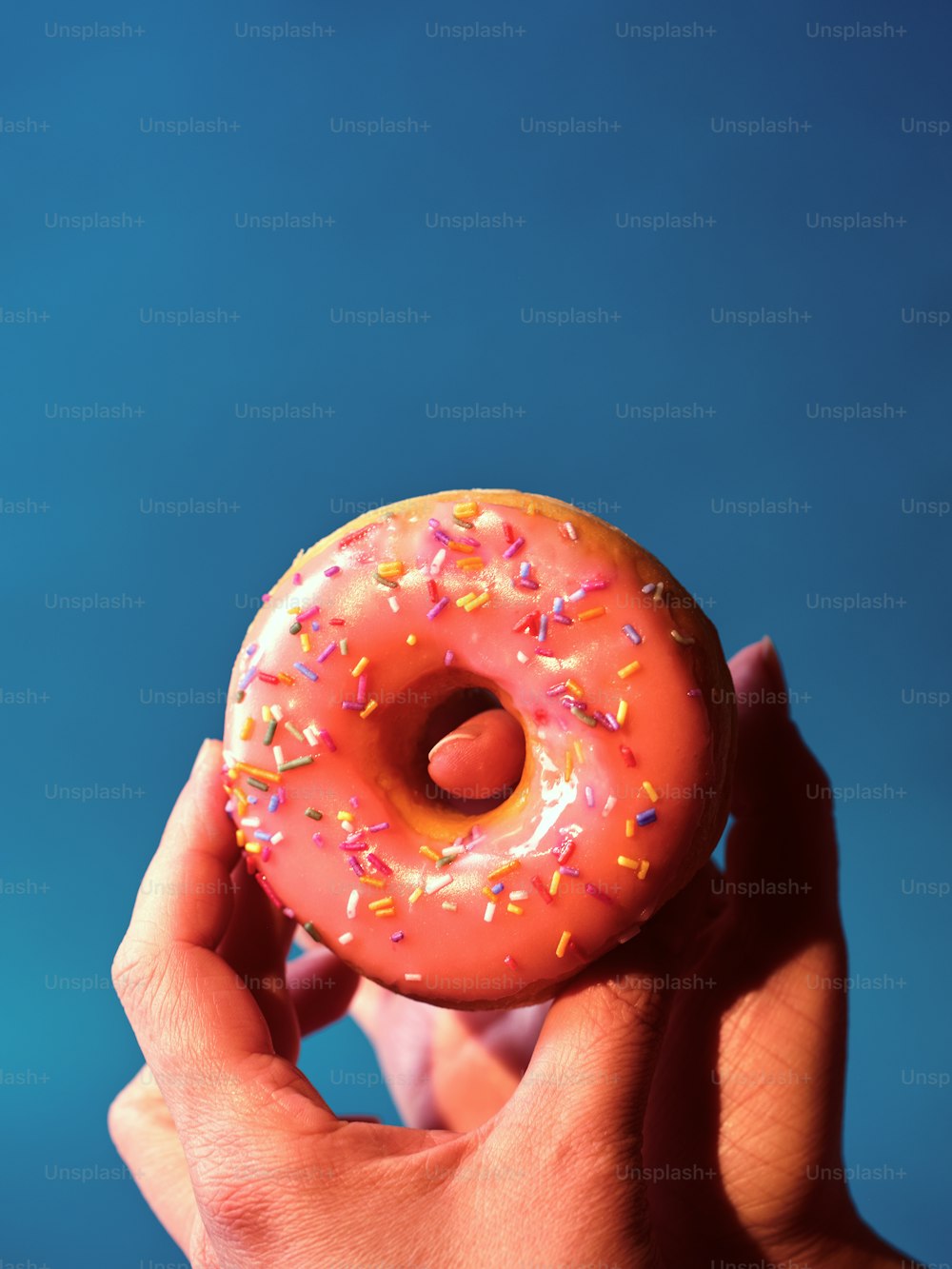 eine Hand, die einen rosa Donut mit Streuseln hält