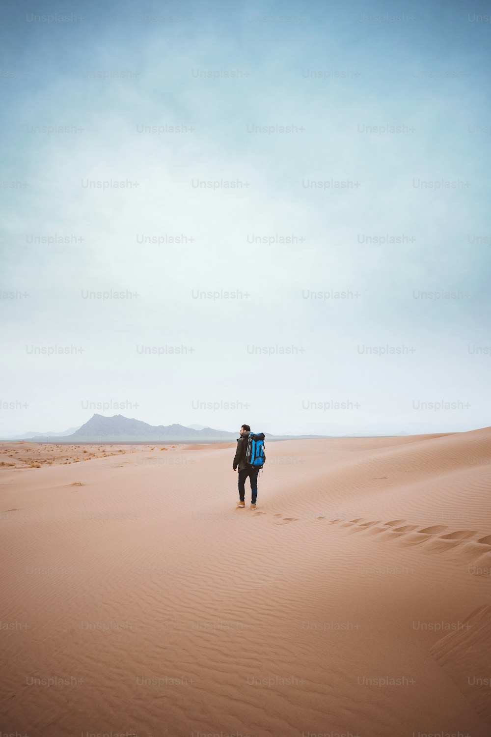 배낭을 멘 남자가 사막을 가로질러 걷고 있다