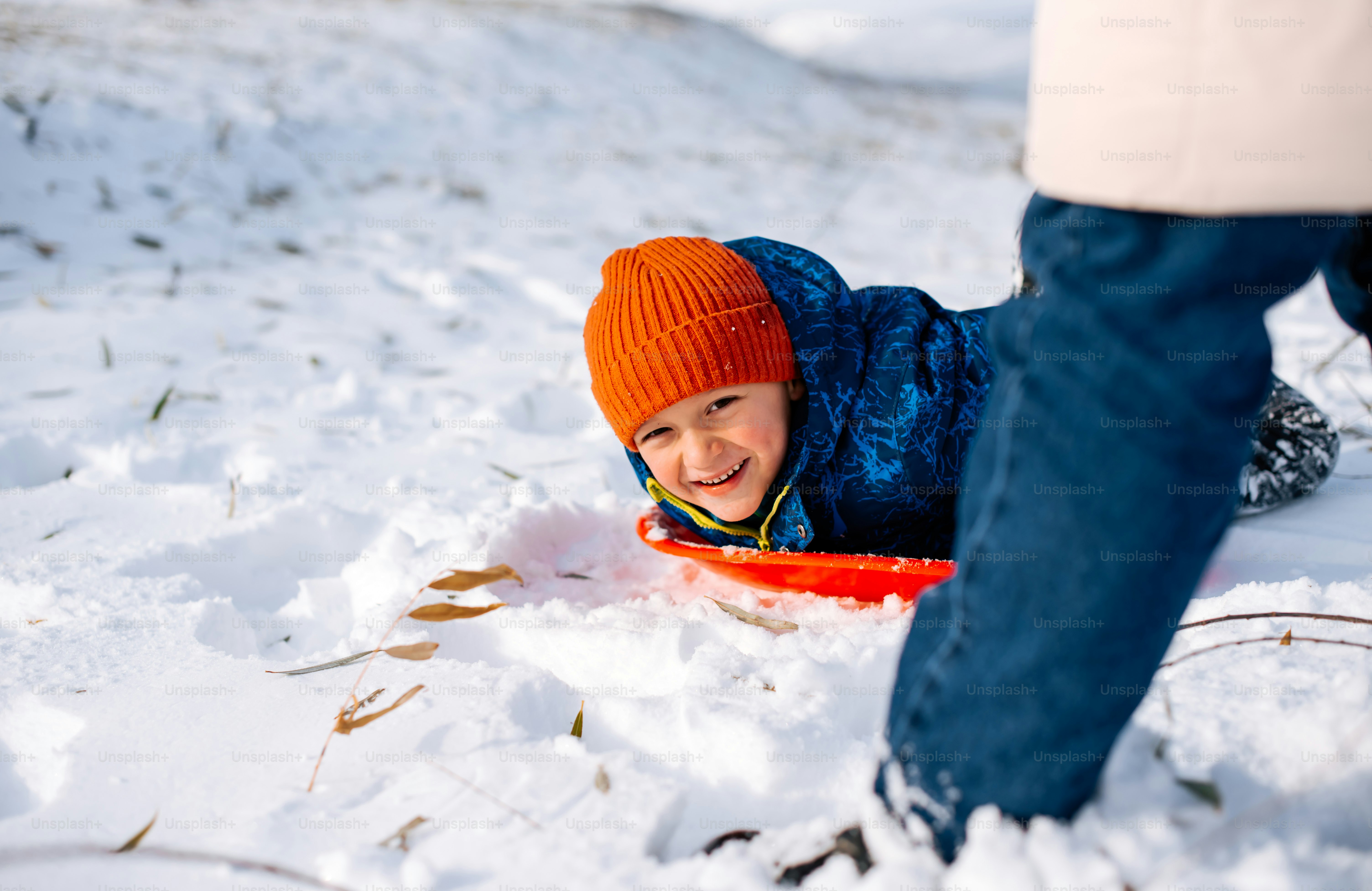 A young boy laying in the snow wearing a blue jacket photo – Snowball ...