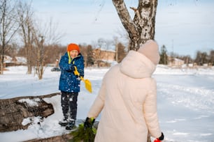 a young boy standing next to a tree in the snow