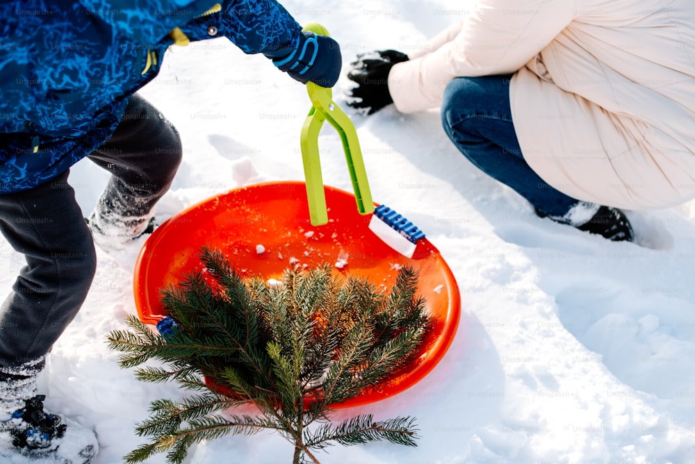 two children playing in the snow with a red bowl