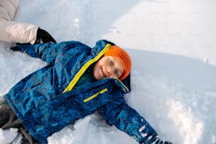 a young boy laying in the snow wearing a blue jacket