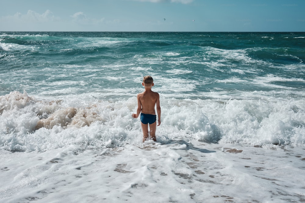 a young boy standing in the surf at the beach