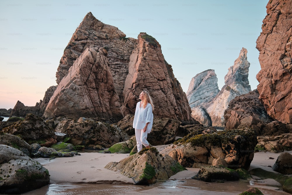 a woman standing on a beach next to some rocks