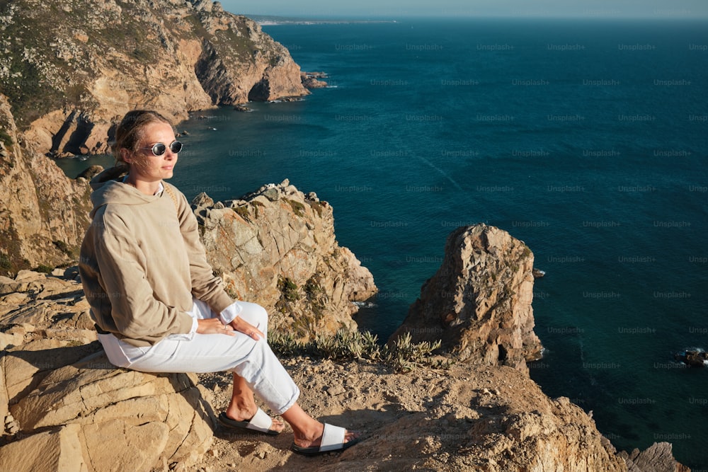 a woman sitting on top of a cliff next to the ocean