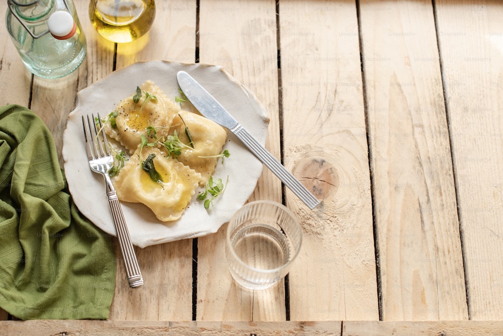 a white plate topped with ravioli next to a glass of water
