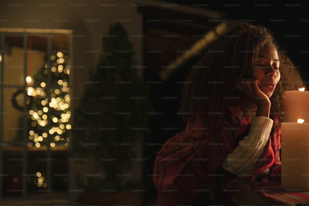 Una donna che tiene una candela accesa davanti a un albero di Natale